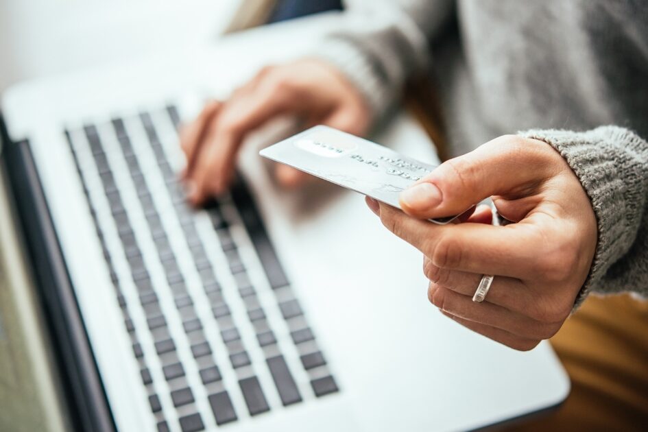 A close up of a person sitting at a laptop, holding a credit card as they type the numbers into the computer