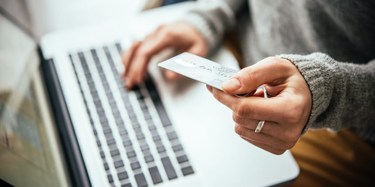 A close up of a person sitting at a laptop, holding a credit card as they type the numbers into the computer